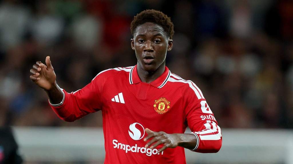 Pemain tengah Manchester United Kobbie Mainoo saat mengenakan pakaian latihan dan tersenyum dalam sebuah acara publik.